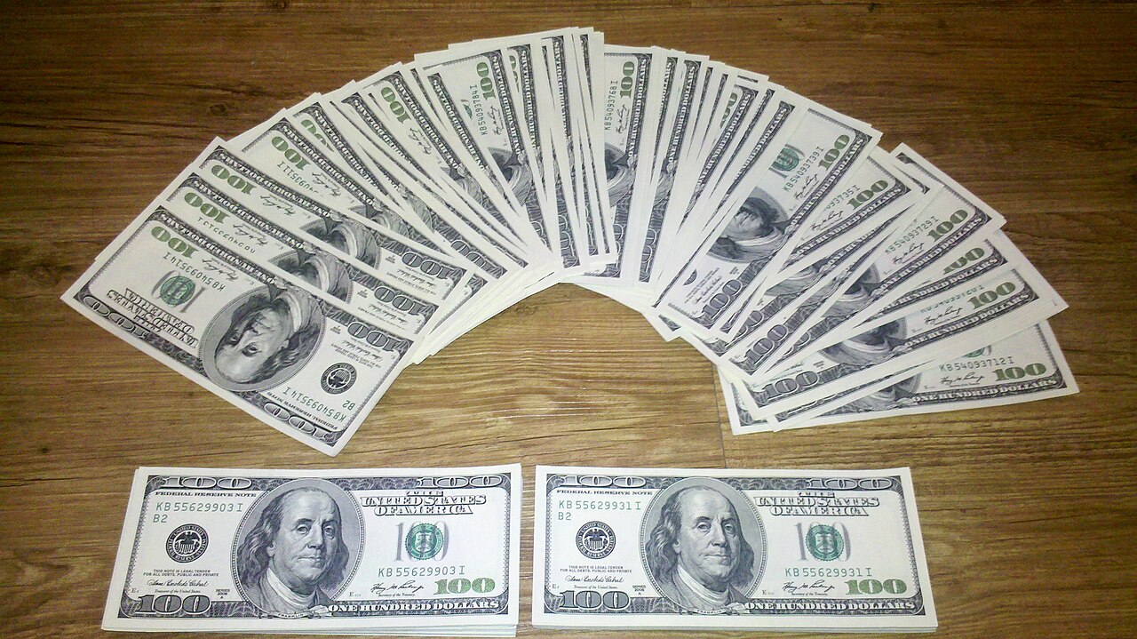 A fan of US hundred-dollar banknotes on a wooden table